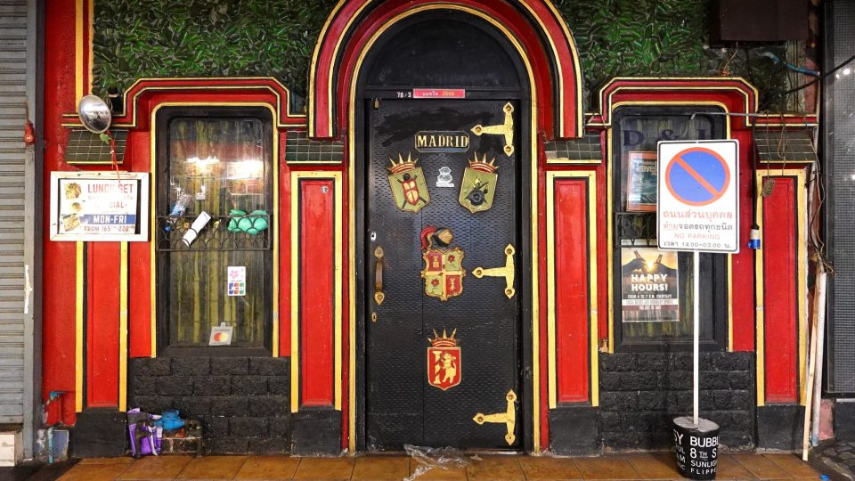 Façade rouge et jaune à arcade, porte noire ornée de blasons et du mot MADRID, mur végétal au-dessus.