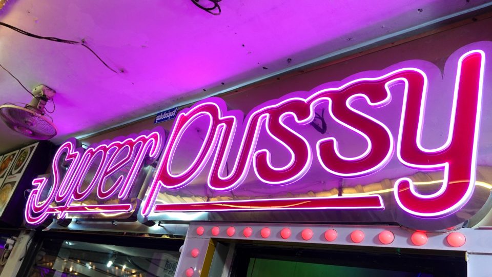 Patpong, un quartier rouge au cœur du centre d'affaires de Bangkok — © Eric Monteil Enseigne au néon rose et violette « Super Pussy » au-dessus de l'entrée d'un bar, bordée d'ampoules rouges.