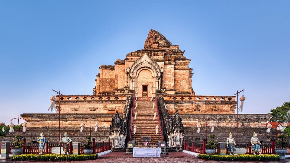 Grand chedi en briques en partie ruiné, avec un escalier central flanqué de nagas et des statues de gardiens au pied.